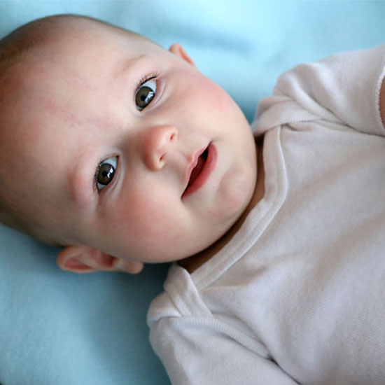 A close up of a baby on a blue banket with eyes open