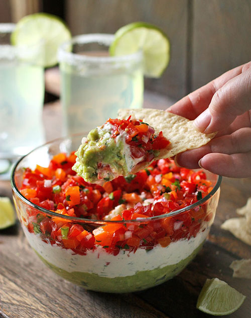 hand dipping a chip into dip with guac, cheese and salsa