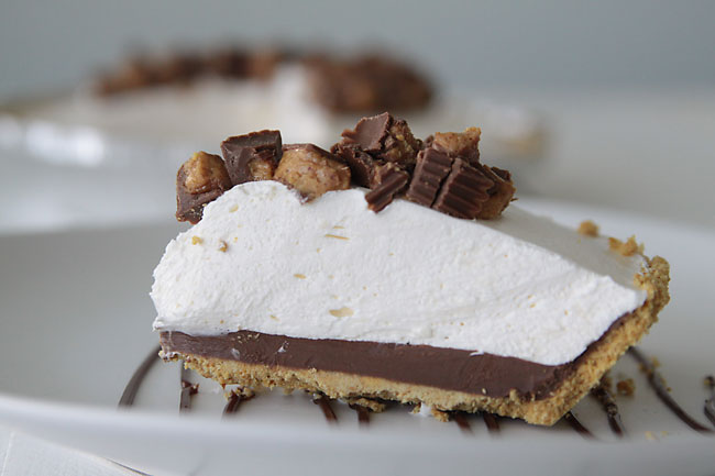 A piece of cheesecake with graham cracker crust, chocolate layer, cheesecake layer, and chopped Reese\'s peanut butter cups