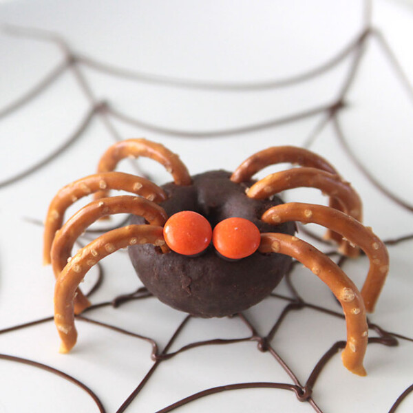 mini chocolate donut decorated to look like a spider with pretzel legs