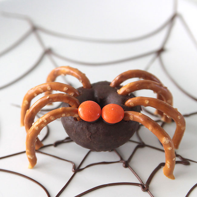 mini chocolate donut decorated to look like a spider with pretzel legs