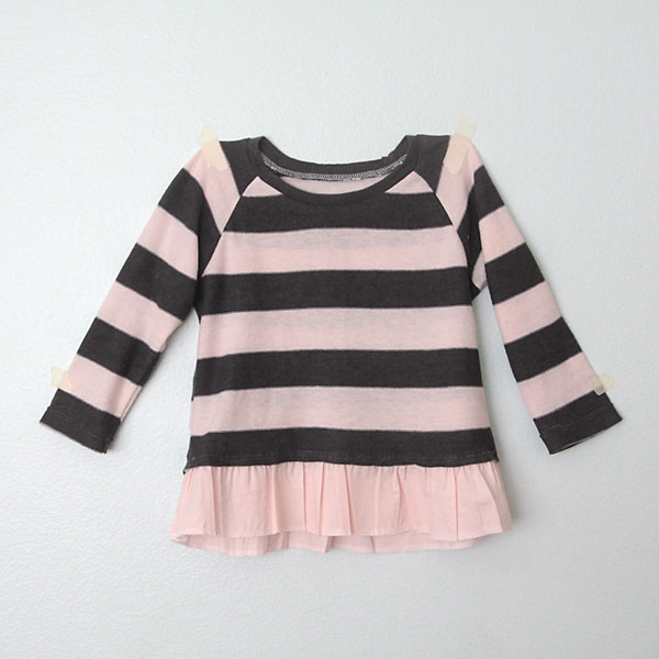 A girl\'s sweater in pink and grey stripes with pink ruffled hem