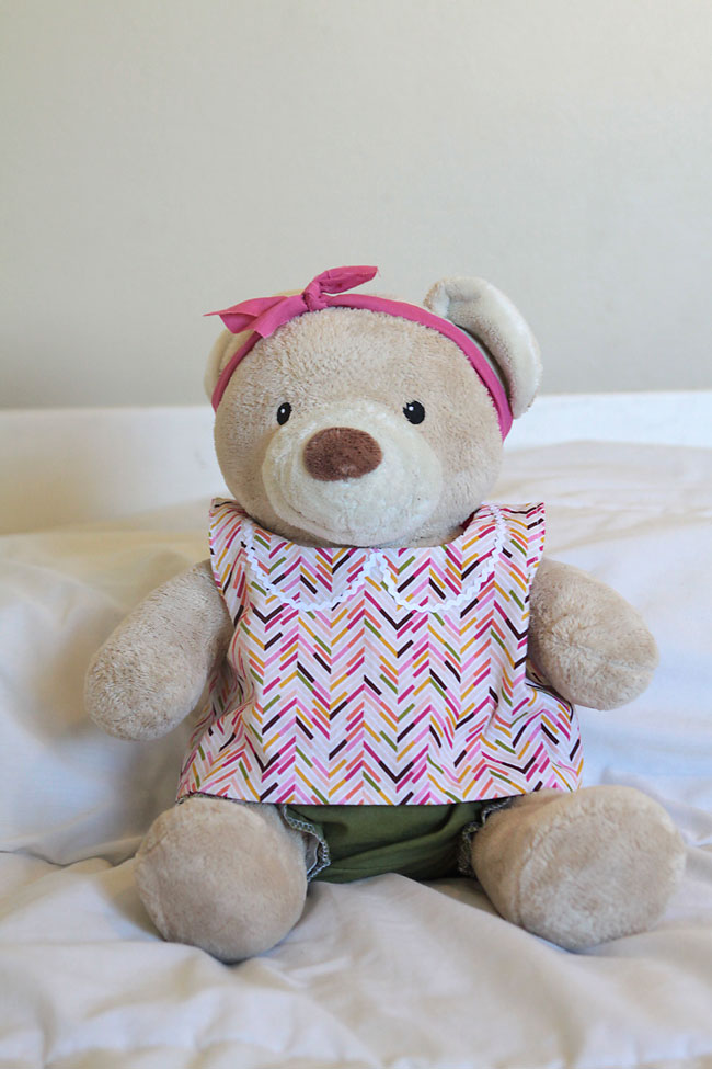 A large brown teddy bear wearing a pink top and green bloomers with a boy around her head