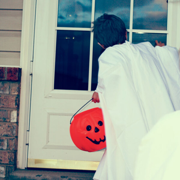 A little boy dressed as a ghost knocking on a door