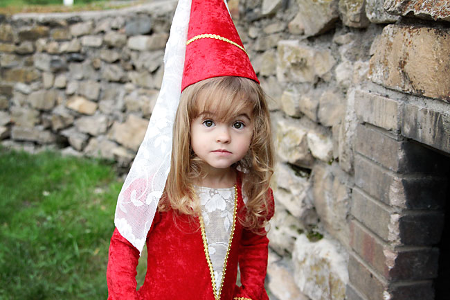 A little girl in a red princess costume in front of a stone wall