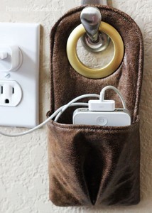 leather phone charger that hangs on a hook near an outlet with pocket for a phone