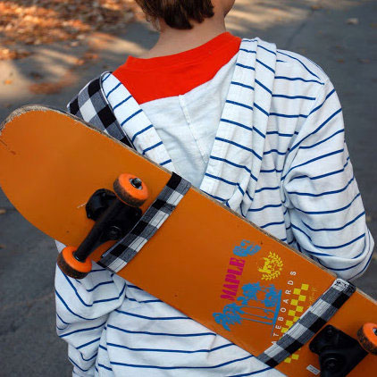 boy carrying a skateboard in a fabric sling