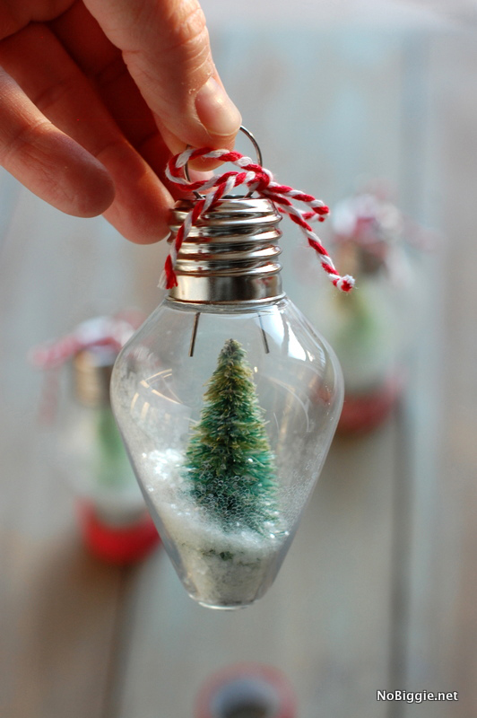 Hand holding a lightbulb shaped Christmas ornament with tiny faux tree and fake snow inside