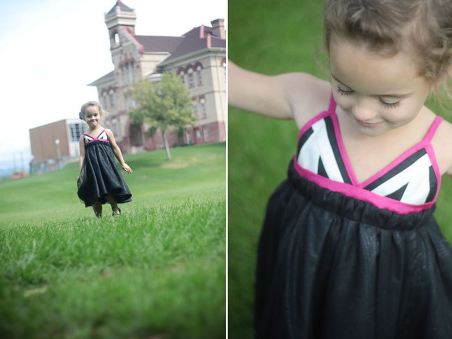 A little girl that is standing in the grass wearing a black dress with pink and white details on the straps