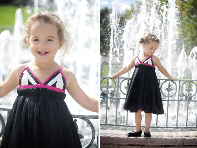 A little girl standing next to a fence wearing a black dress