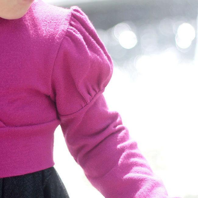 A girl wearing a pink sweater with puffed sleeves