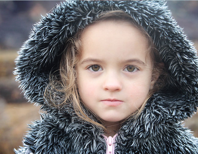 A close up of a little girl with a faux fur hood