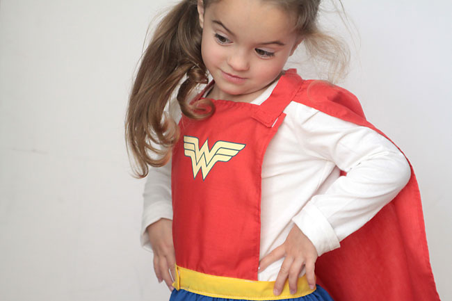 A little girl wearing a superhero cape and skirt