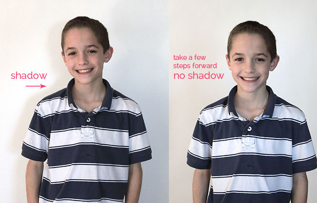 boy standing in front of a white background casting a shadow; boy moved forward in front of the background so he doesn\'t cast a shadow