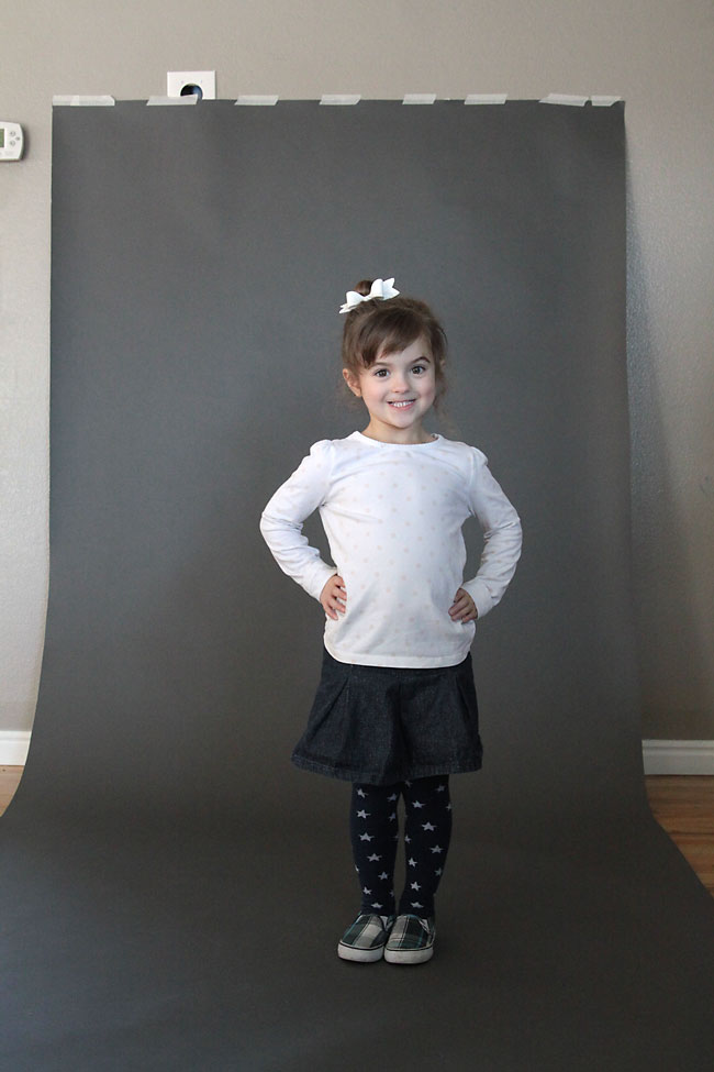 A girl standing in front of grey seamless background paper that\'s taped to the wall