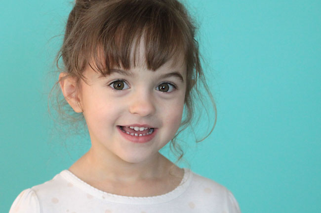 A girl smiling for the camera with turquoise Seamless Paper behind her
