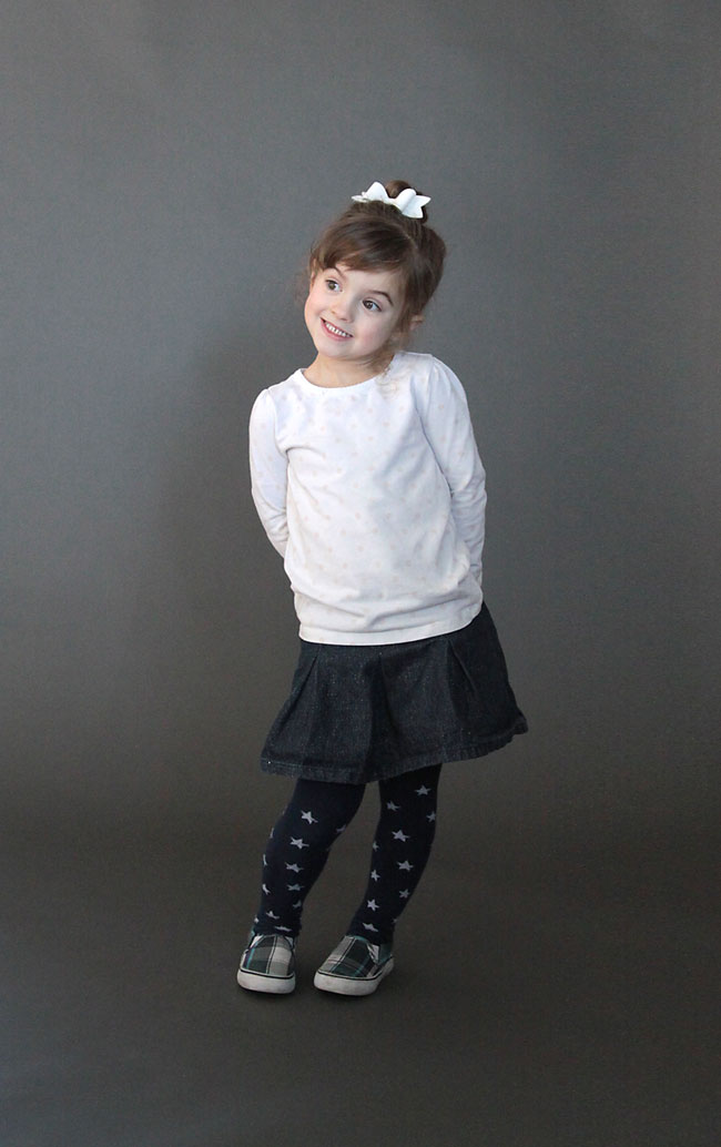A little girl standing in front of a plain grey background