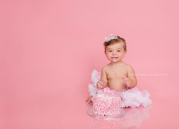 A little girl baby eating a cake with a pink background