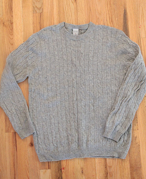 A grey cable knit sweater on a wooden surface