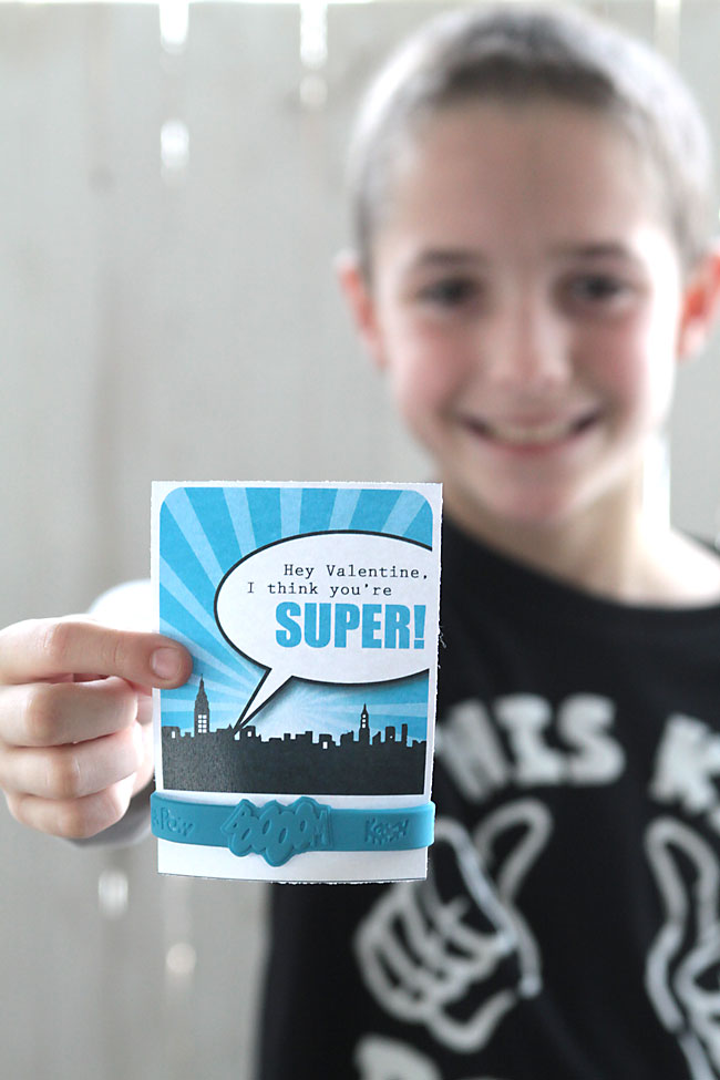 A boy holding a blue superhero valentine\'s day card with a superhero bracelet