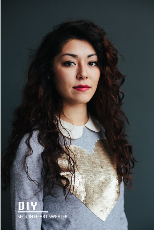 A woman wearing a grey sweater with a large gold heart on it