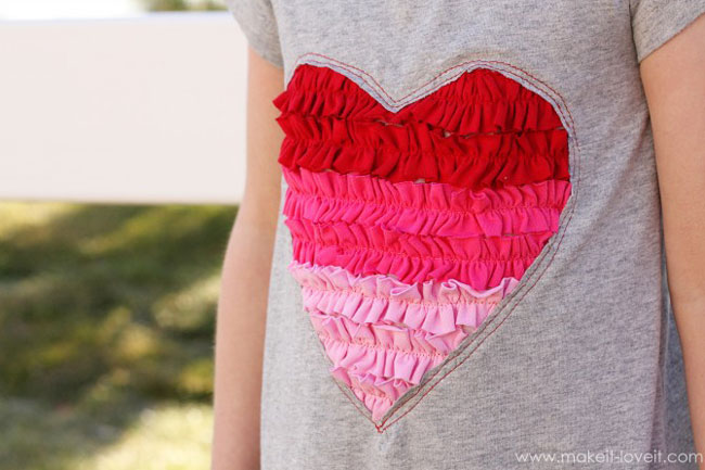 A grey valentines day shirt with a heart made from ruffled fabric strips on it