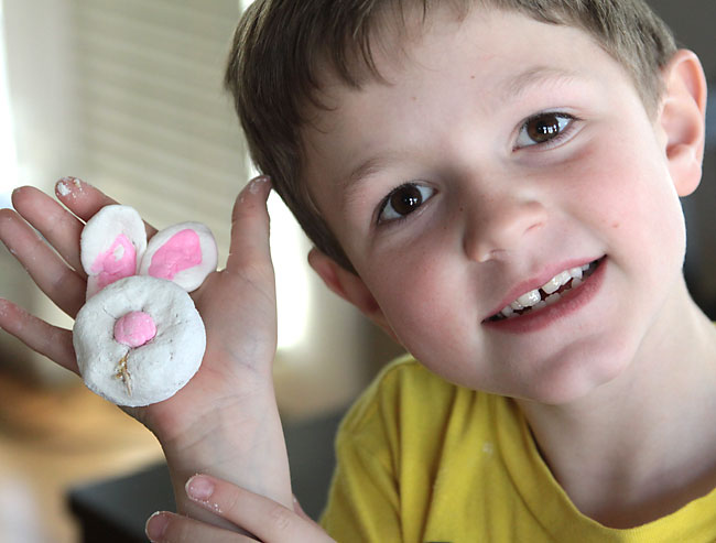 A boy holding a powdered donut decorated to look like a bunny