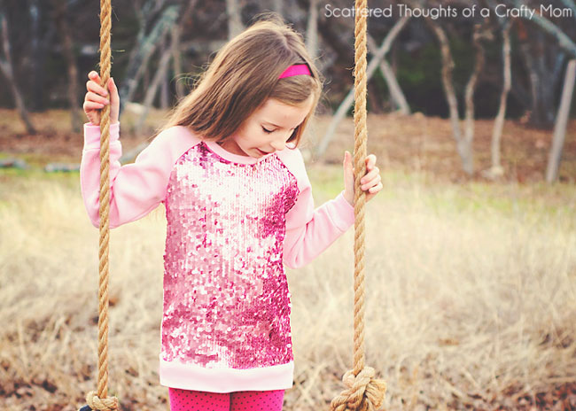A little girl standing in a swing wearing a long sleeve raglan shirt with sequins