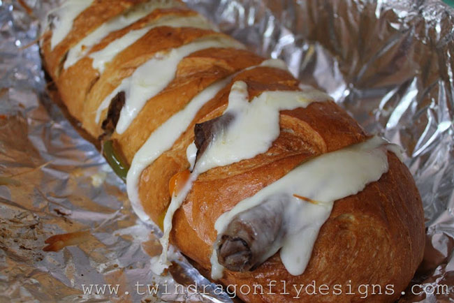 A loaf of french bread with roast beef and cheese tucked into slices wrapped in foil and cooked in the campfire
