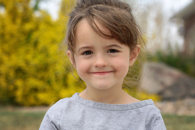 A little girl smiling at the camera with blurred yellow flowers in the background