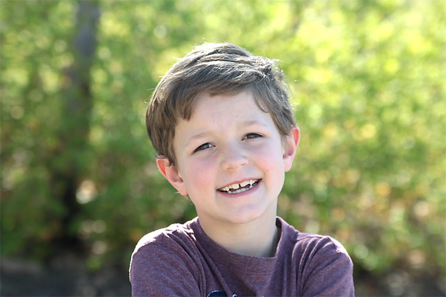 A young boy in front of leaves that are blurred in the background
