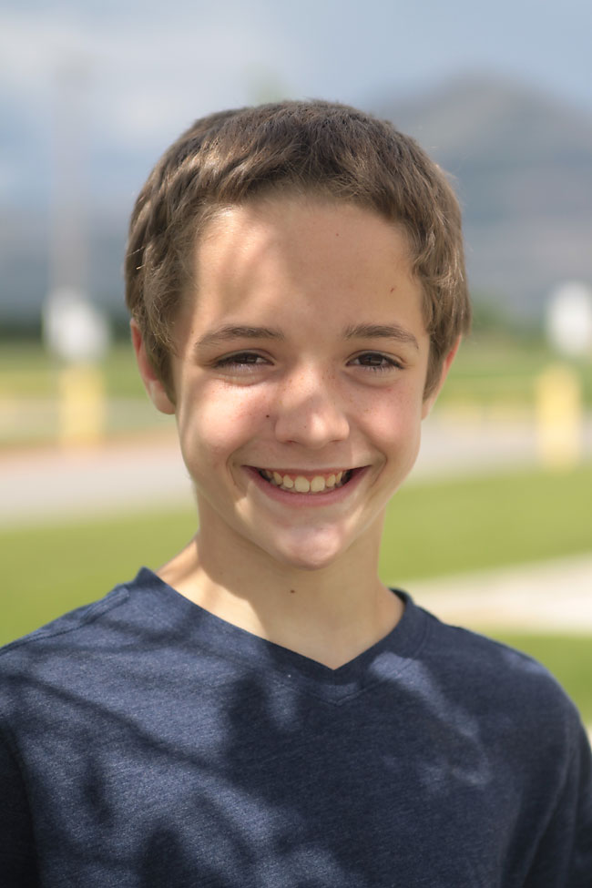 A young boy standing outside with dappled shadows on his face