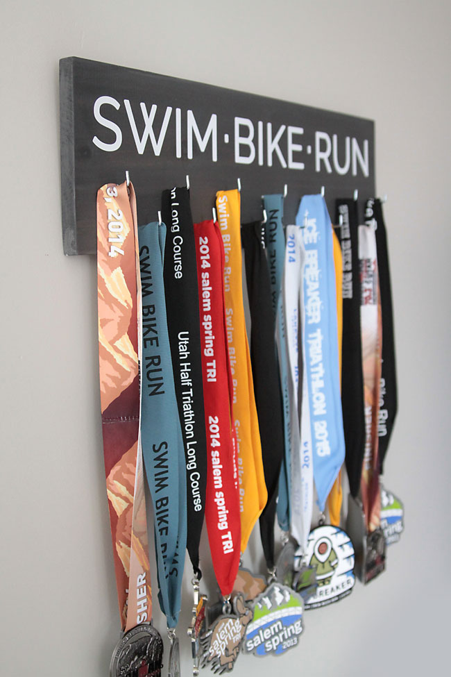 Sign that says swim bike run with race medals hanging from it