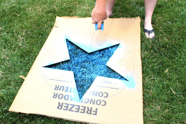 A person using a template to spray paint stars on the grass