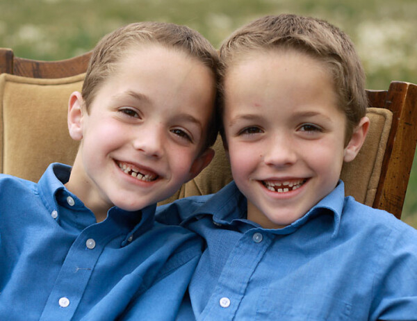 Two siblings sitting in a chair in a field smiling