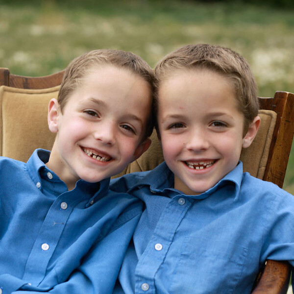 Two siblings sitting in a chair in a field smiling