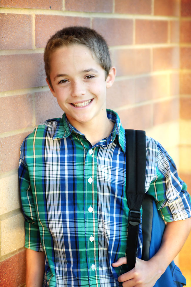 Boy with a backpack leaning against a wall