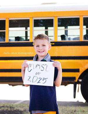 A boy in front of a schoolbus with a sign that says class of 2025