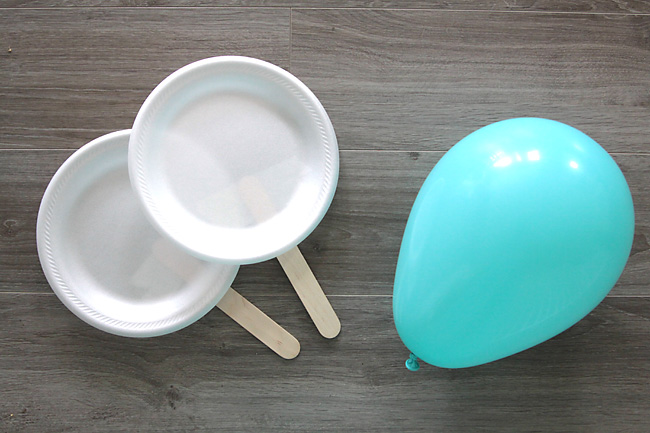 Paper plates with popsicle sticks tape on as handles and a blown up balloon