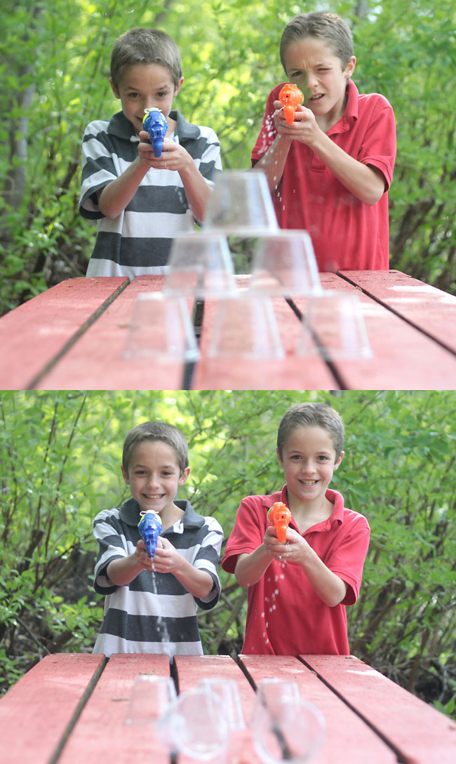 Boys shooting water guns at a stack of plastic cups