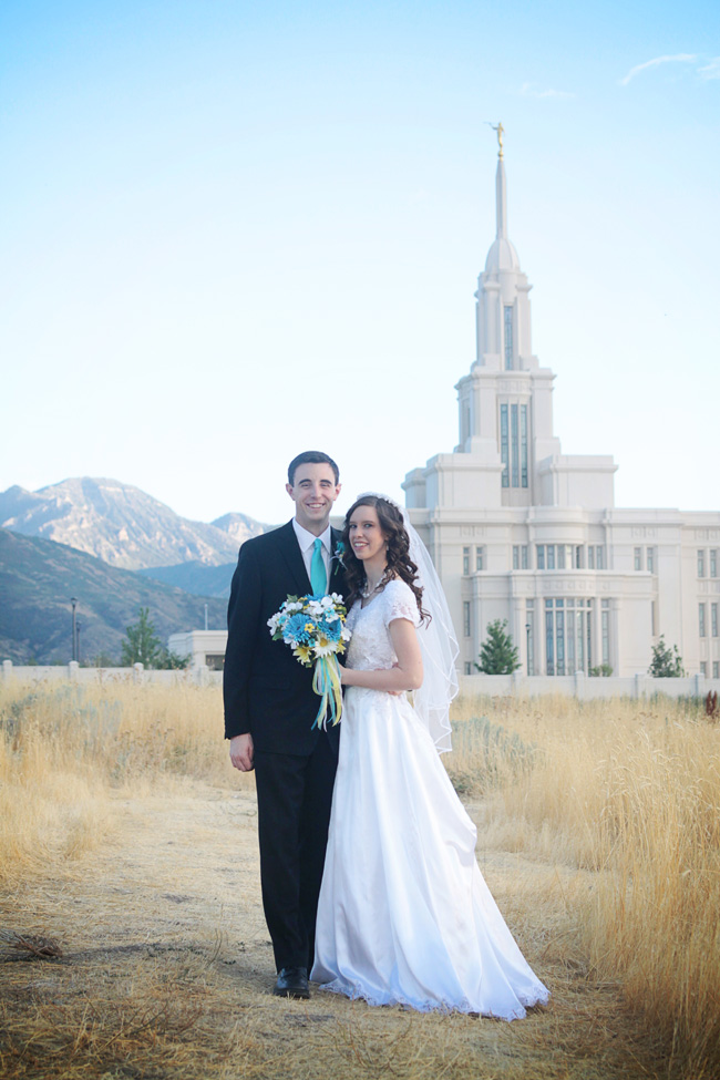 Bride and groom standing in a field in front of the temple they were married in