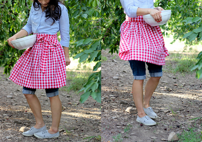A girl standing in an orchard with a red and white gingham half apron