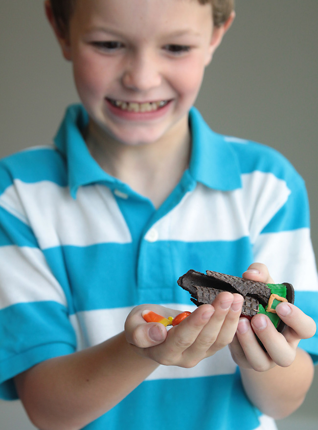 A little boy that is holding a broken witch hat cookie with candy spilling out