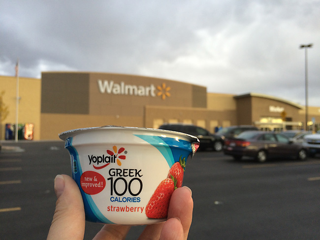hand holding a greek yogurt cup in front of a Walmart store