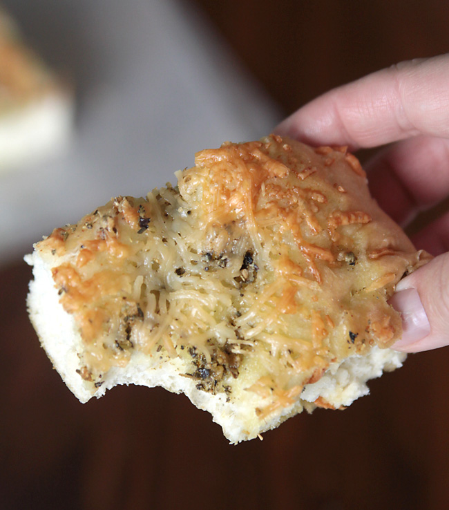 A hand holding a piece of focaccia with a bite taken out of it