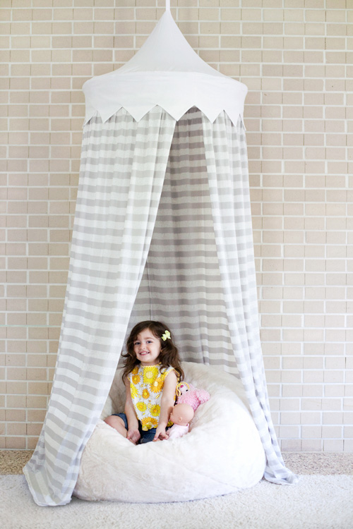 A girl sitting on a bean bag with a fabric canopy hanging from above her