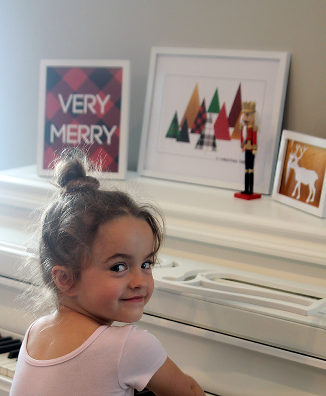 Framed Christmas prints on a piano with a little girl sitting at the piano