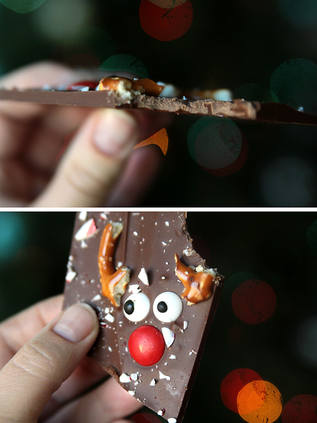Hand holding piece of chocolate with pretzels, eyes and red M&M to make reindeer face