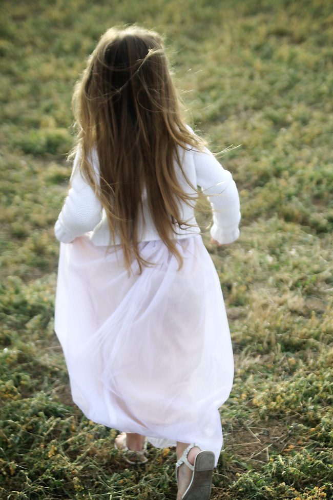 A girl walking through a green field in a long skirt