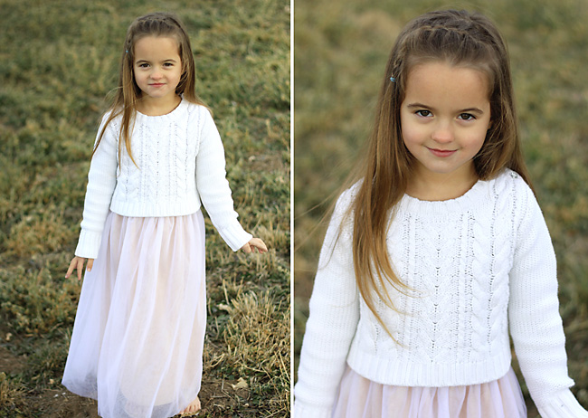 A little girl that is standing in the grass wearing a white sweater and light pink skirt